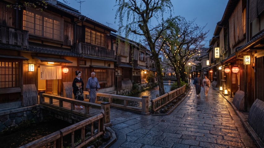 石畳の路地と川沿いに佇む伝統的な料亭街を歩く人々の様子
