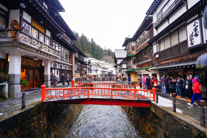 川沿いに重厚な木造温泉旅館が立ち並び風情ある食体験を連想させる昼の銀山温泉街